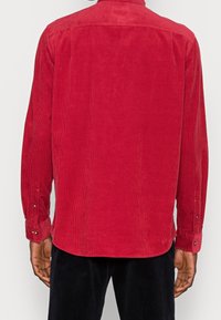 Camisa de pana roja con mangas largas, acanalada verticalmente, con cierre de botones en los puños y un diseño de cuello clásico.