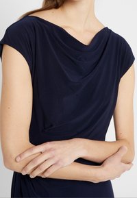 Vestido drapeado de color azul marino, confeccionado en una tela suave y elástica, con escote barco y mangas cortas, que presenta pliegues sutiles y una cintura ajustada.