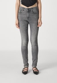 Jeans ajustados grises hechos de denim, con cinco bolsillos, una cintura estándar y una textura suave. Llevados con zapatos planos negros de punta.