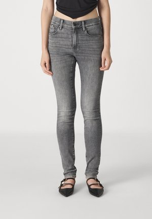 Gray slim-fit jeans made from denim, featuring five pockets, a standard waistband, and a smooth texture. Worn with black pointed flats.