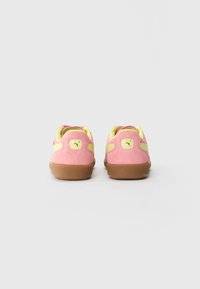 Et par rosa semskede sneakers med gule detaljer og gummisåler, sett fra baksiden på en enkel hvit bakgrunn.