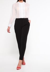 Vit blus med knäppning fram och spetsdetaljer, matchad med svarta avsmalnande byxor. Accenterad med röda sandaler. Mjuk tygkvalitet.