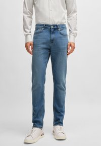 Light blue jeans made of denim, featuring a regular fit, five pockets, and subtle stitching details. Paired with white sneakers.