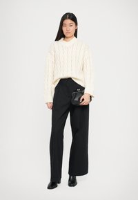Pull en tricot blanc chunky, pantalon noir à jambes larges, sac à main noir avec fermoir et bottes à talons noires ; design épuré et motif de tricot texturé.