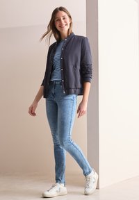 Chaqueta bomber acolchada navy, camiseta a rayas, jeans de color azul claro y zapatillas blancas con detalles grises; tejido suave y corte casual.