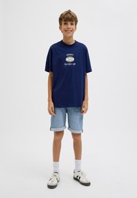 T-shirt in cotone blu navy con maniche corte e scollatura rotonda, caratterizzata da un logo stampato e testo. Abbinata a pantaloni corti in denim blu chiaro.