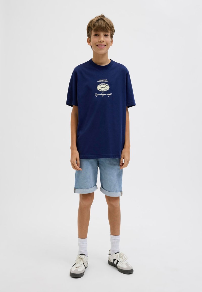 T-shirt in cotone blu navy con maniche corte e scollatura rotonda, caratterizzata da un logo stampato e testo. Abbinata a pantaloni corti in denim blu chiaro.