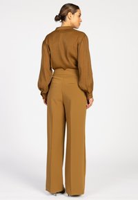 Brown long-sleeve blouse with balloon sleeves paired with high-waisted, wide-leg trousers in a matching warm brown shade. Smooth texture.