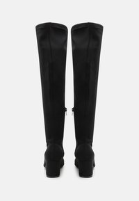 Botas negras sobre la rodilla, fabricadas con material sintético suave. Tacones cuadrados con cierres de cremallera en la parte posterior para facilitar su uso.