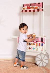 Carrito de helados con un toldo a rayas rosas, que presenta gráficos de helados coloridos. Niño sosteniendo un cucurucho de helado, vestido con una camiseta clara y pantalones cortos.