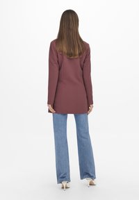 Mauve blazer med långa ärmar, skräddarsydd passform, kombinerad med ljusblå utsvängda jeans och vita klackar, sedd bakifrån.