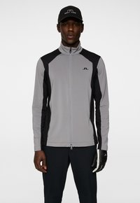 Szara i czarna kurtka z suwakiem z półgolfem, dopasowany krój i kontrastowe rękawy; w zestawie z czarną czapką i rękawiczką.