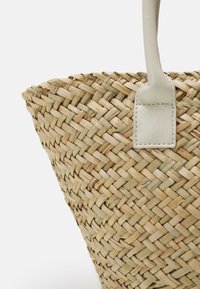 Flettet stråkurv med en konisk form, der har en lys beige farve og et glat hvidt læderhåndtag med en rektangulær fastgørelse.