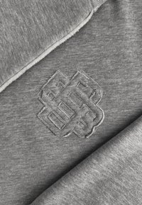 Grijze sweatshirt met een geborduurd knoopontwerp in een bijpassende kleur. De stof heeft een zachte, gladde textuur met een licht rafelige rand.