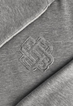 Sweatshirt gris avec un design de nœud brodé dans une teinte assortie. Le tissu présente une texture douce et lisse avec un bord légèrement effiloché.