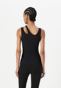 Svart ribbet tank topp med et unikt design med doble skulderstropper, tettsittende silhuett og en jevn tekstur. Kombinert med svarte leggings.