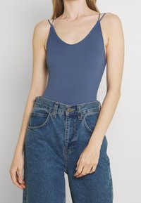 Niebieski prążkowany body z cienkimi ramiączkami, w połączeniu z wysokimi, wyblakłymi niebieskimi dżinsami z zapięciem na guzik i bocznymi kieszeniami.