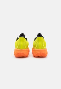 Neon gule træningssko med en struktureret orange sål, der har en sort indvendig kant og et minimalistisk design. Bagfra viser de glatte former.