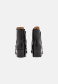 Botas de tobillo de cuero negro con un acabado liso, cremalleras laterales y un tacón bajo en bloque. El interior cuenta con un forro marrón contrastante.