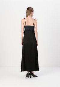 Svart maxi-kjole med tynne stropper, en tettsittende bodice og en flytende skjørt; har en teksturert stoff og en glidelås på baksiden.
