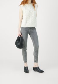 Vitt stickat ärmlöst linne med strukturerat mönster, grå slim-fit jeans, svart plisserad handväska och svarta öppna klackskor.