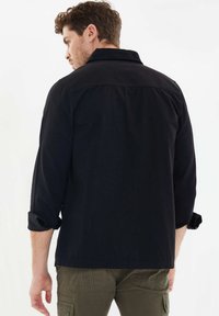 Zwart, langwerpig shirt met een klassieke kraag en opgerolde mouwen, gemaakt van katoen. Achteraanzicht, naadloos ontwerp, geen zichtbare details.