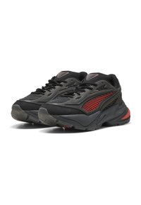 Sneaker sportive nere con accenti rossi, superiori in rete testurizzata, suola in gomma e elementi di design a strati. Presentano lacci neri e dettagli di branding.
