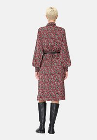 Robe à manches longues avec imprimé floral rouge, taille ceinturée et accents noirs. Présente une silhouette fluide et une coupe mi-genou. Tissu texturé.