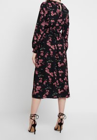 Black midi dress with long sleeves, floral print in pink and green, cinched waist, keyhole back detail, paired with black strappy heels.