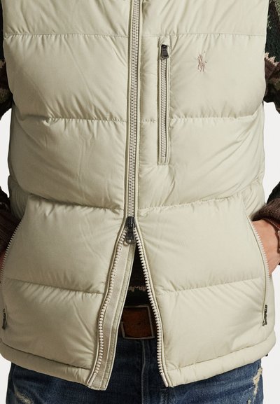 Colete puffer bege claro com costura horizontal, dois bolsos com fecho zip e fecho com zíper. Apresenta um pequeno logótipo no peito.