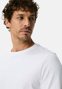 Wit T-shirt met ronde hals in een zachte, gladde stof. Heeft een subtiel logo op de borst en korte mouwen. Strak, minimalistisch ontwerp.