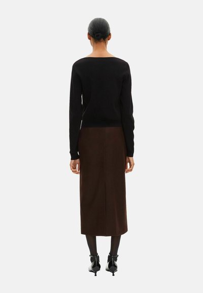 Sort trøje og brun nederdel, set bagfra. Trøjen er tætsiddende, med lange ærmer og en bred halsudskæring. Nederdelen er knælængde med en slids bagpå.