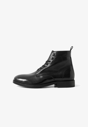 Schwarze Leder-Ankle-Boots mit glänzender Oberfläche, Schnürung an der Vorderseite, sechs Ösen und einem Zugschlaufen hinten. Flache Gummisohle.