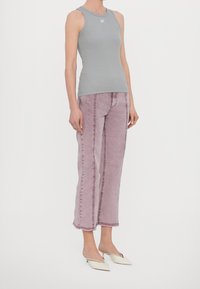 Szary top bez rękawów z zaokrąglonym dekoltem, zestawiony z różowymi dżinsowymi spodniami o lekko zniszczonym wykończeniu i widocznym przeszyciu.