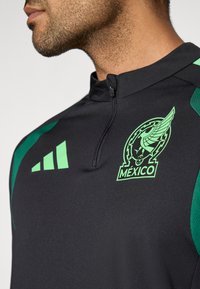 Melna sporta jaka ar zaļām akcentēm. Ir rāvējslēdzēja apkakle, Meksikas logotips un trīs zaļas svītras uz kreisā pleca.