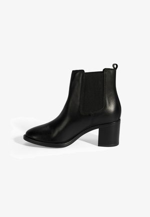 Bottines en cuir noir, avec des panneaux élastiques sur les côtés, bout pointu et talon bloc. Elles sont dotées d'une languette à l'arrière pour un enfilage facile.