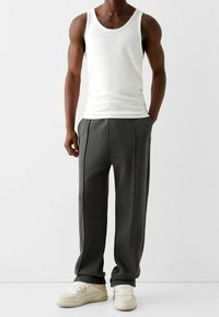 Débardeur en coton blanc associé à un pantalon de jogging gris avec des plis subtils et des poches latérales. Porté avec des baskets blanches.