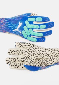 Due paia di guanti: uno blu con grip in silicone testurizzato e dettagli a pois, l'altro crema con macchie nere. Entrambi presentano un design aderente.