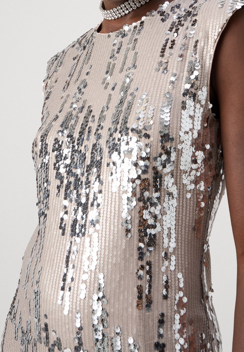 Gros plan d’une personne portant une robe beige avec des paillettes argentées et un collier ras-du-cou en strass sur peau nue.