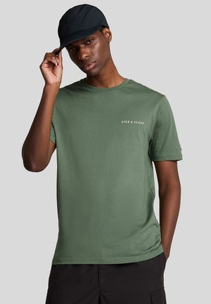 Grøn bomulds t-shirt med korte ærmer, rund hals og lille hvid tekstlogo på brystet, parret med en sort cap.