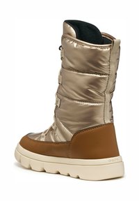 Bota con parte superior de nailon dorado metálico, acentos de cuero marrón, caña acolchada y suela de goma blanca. Presenta cordones y una tira de sujeción.