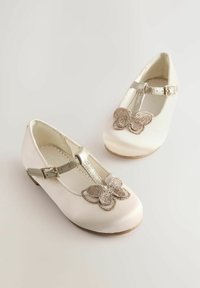 Weiße Satin-T-Strapschuhe mit einer metallischen Schnalle und einem dekorativen Schmetterling-Accessoire aus metallic-garn auf der Zehenpartie. Flache Sohle, abgerundetes Design.