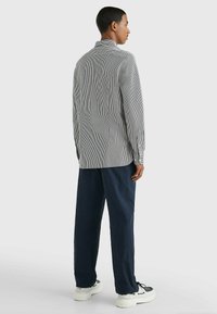 Camisa de manga larga a rayas en blanco y negro, con un cuello clásico. Combinada con pantalones sueltos azul marino y zapatillas blancas.