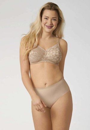 Donna sorridente con lunghi capelli biondi che indossa un reggiseno in pizzo beige e biancheria intima coordinata con finitura liscia su uno sfondo chiaro e uniforme.