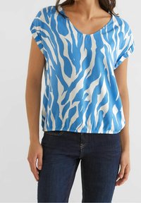 Top azzurro e bianco a maniche corte con scollo a V, caratterizzato da un motivo a strisce zebra e una vestibilità rilassata, realizzato in tessuto morbido. Abbinato a jeans scuri.