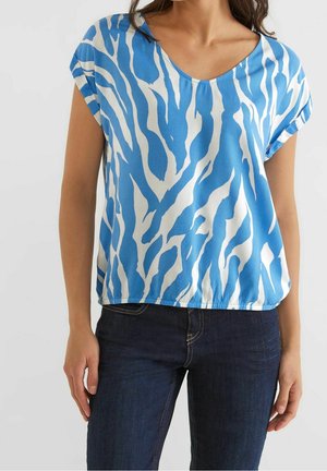 Blauw-witte top met korte mouwen en een V-hals, voorzien van een zebrapatroon en een ontspannen pasvorm, gemaakt van zachte stof. Gecombineerd met donkere jeans.