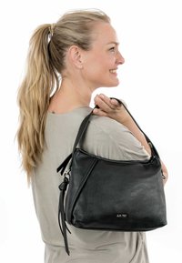 Mustankynä kasvi, pehmeä muoto, kaksivöinen, koristeellinen tupsu kiinnitettynä. Ei näkyviä suuria varusteita tai logoja.