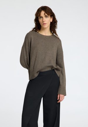 Pull en tricot marron à côtes avec un large col rond et des épaules tombantes, associé à un pantalon noir élégant à wrap avec un détail de bouton.