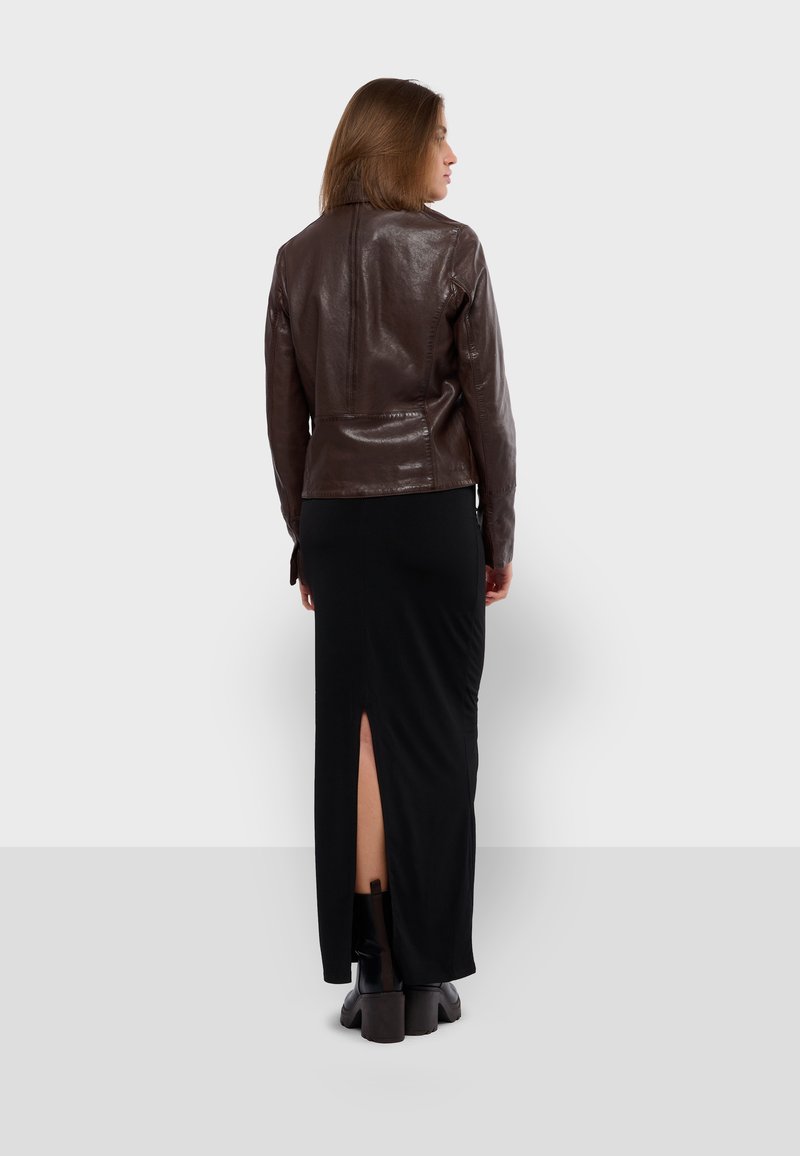 Brązowa skórzana kurtka o dopasowanym kroju, noszona na czarnej maxi sukience z rozcięciem do ud. Czarne, masywne botki dopełniają stój.