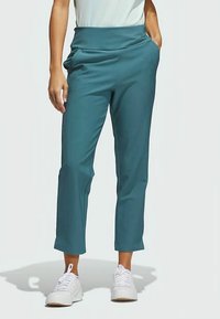 Teal cropped pants with a wide, folded waistband and side pockets, made from a smooth fabric. Worn with white sneakers.